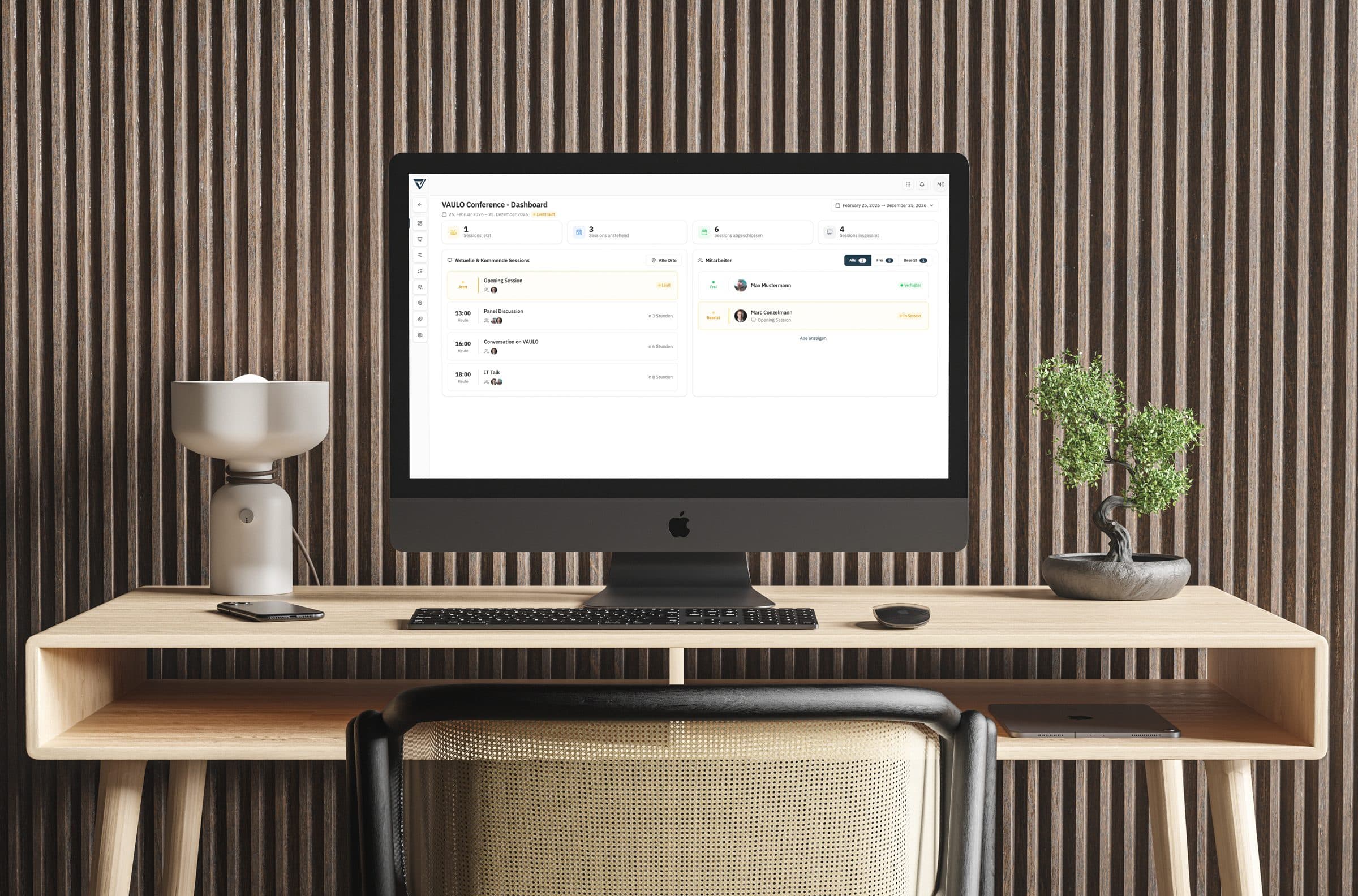 VAULO Events on a desk monitor — the conference dashboard with sessions, times and the staff status