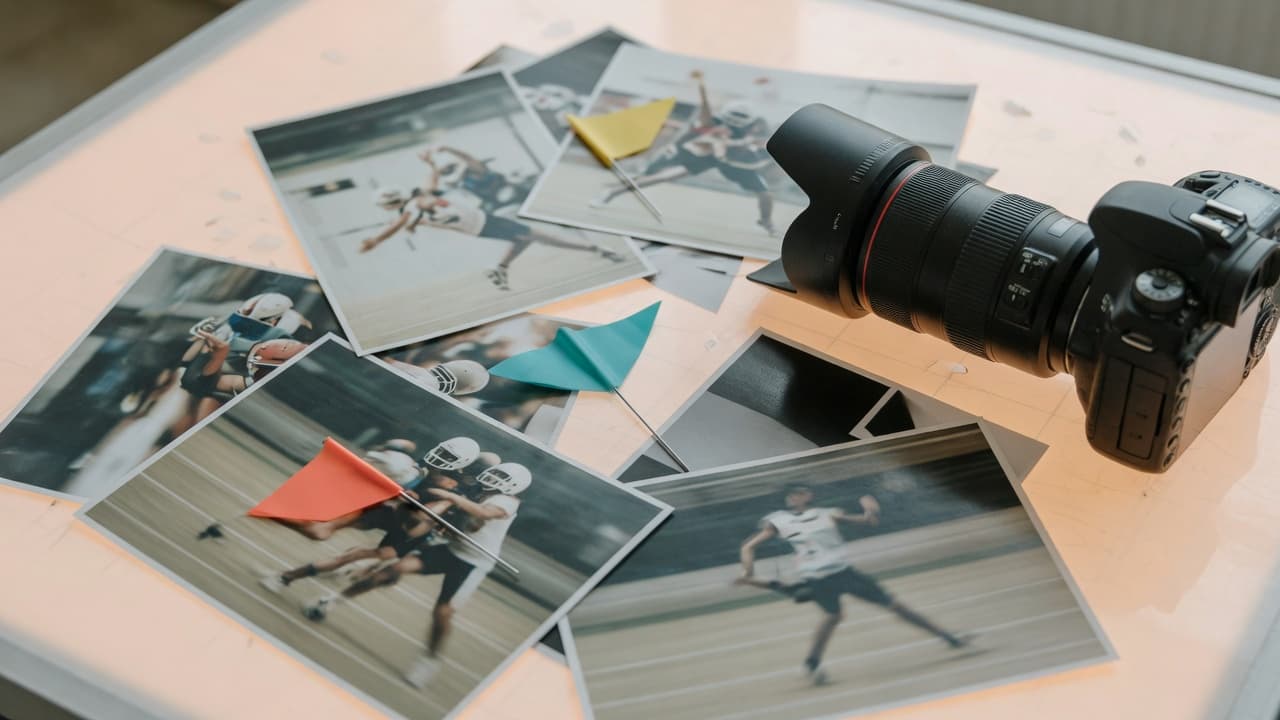 A telephoto camera and sports prints with marker flags on a light table