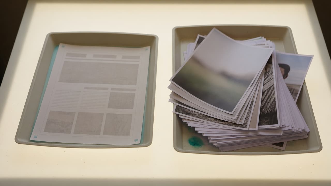 Two trays on a light table — one holding a web page proof, one holding a stack of prints